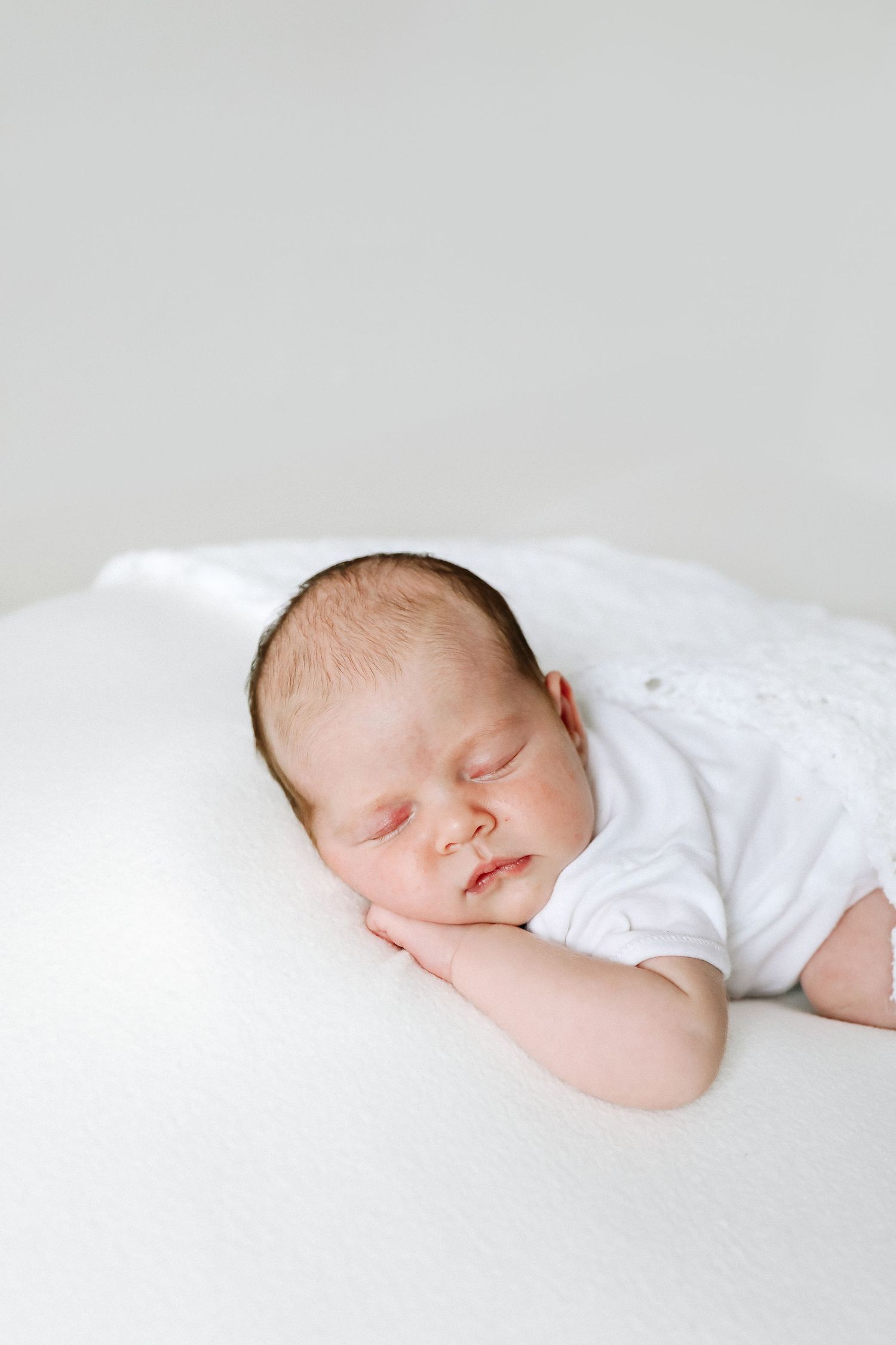 A newborn baby sleeps peacefully on white bedding in soft, natural lighting, during newborn photoshoot in Nottingham