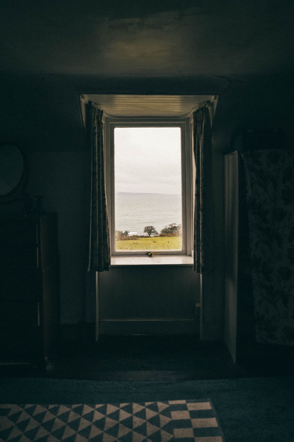 View through a dark window frame looking out at a serene coastal landscape with trees on the horizon.