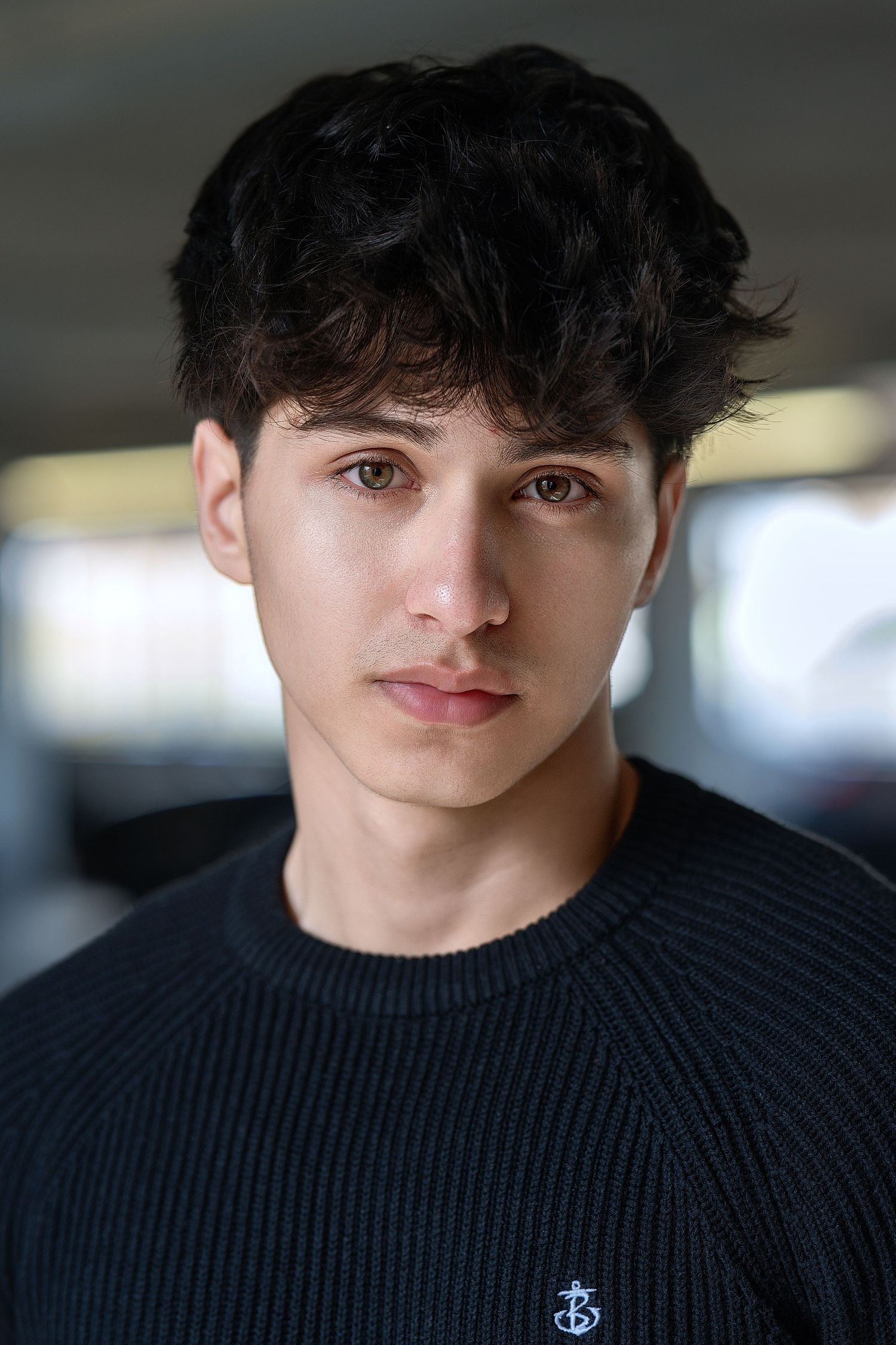 Portrait of someone wearing a black knit sweater with dark tousled hair and a high contrast studio lighting setup.