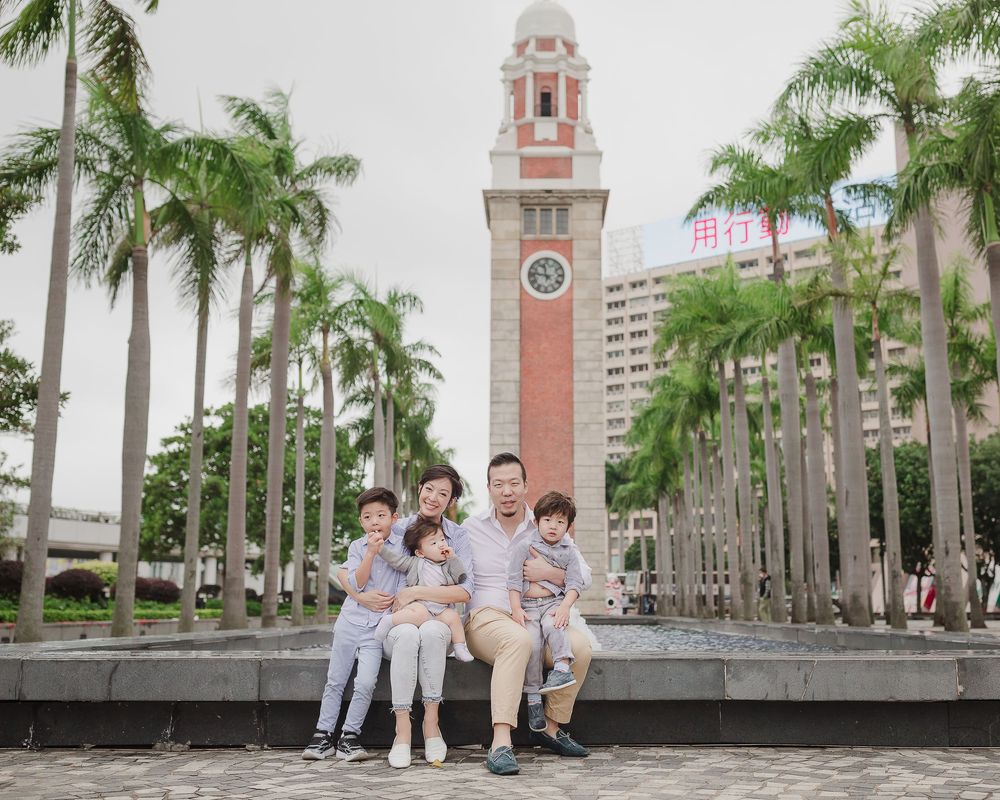 Four connected photos show people posing in front of a clock tower surrounded by palm trees.