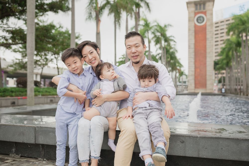 A family sits together by a fountain with palm trees and a clock tower in the background.
