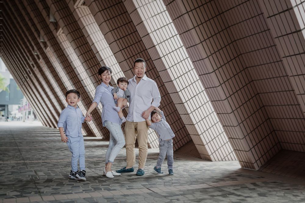 Family poses together under a modern architectural structure with angled white walls on a sunny day.
