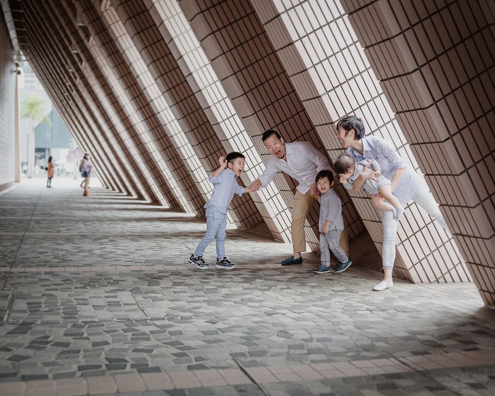 Four photographers capture photos in a modern architectural corridor with dramatic diagonal pillars and stone floor.