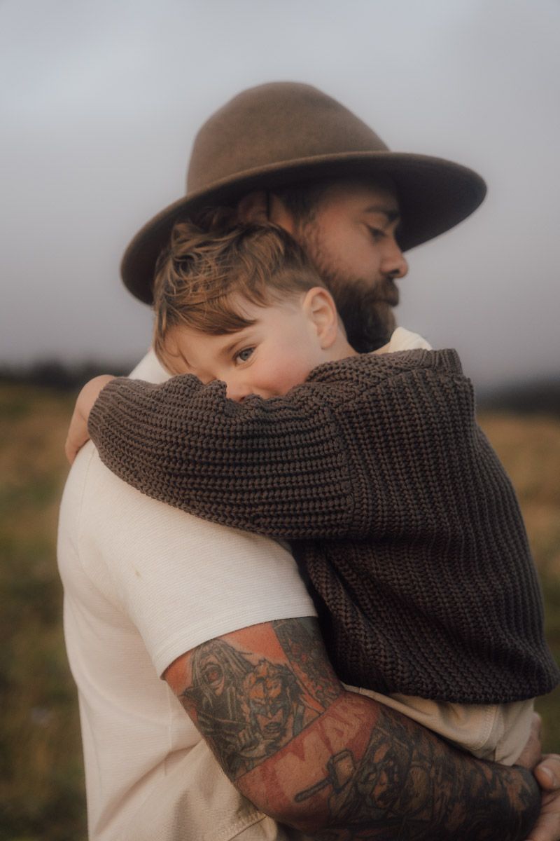 Two people in warm clothing share an intimate embrace against a moody outdoor backdrop.
