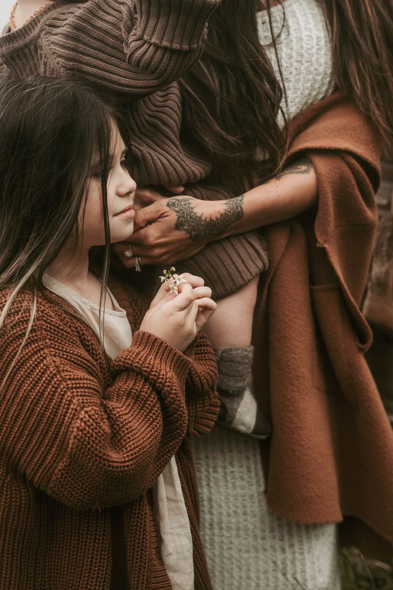 Two people in brown knit sweaters share an intimate moment against a neutral backdrop in warm, moody lighting.