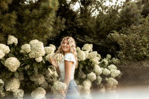 A person posing by blooming white hydrangea bushes in dramatic lighting.