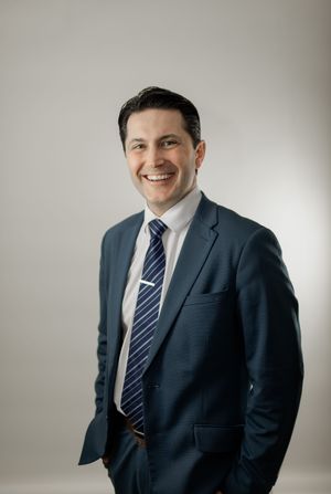 Professional in a dark suit and striped tie poses against light background in series of business headshots.
