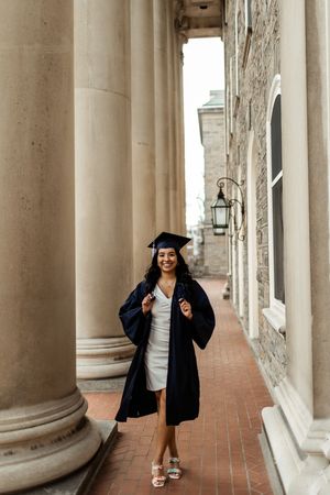 A graduation photoshoot in a classical colonnade hallway with white columns and brick floor.