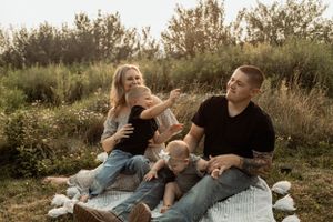Family relaxing together on picnic blanket in tall grass during sunset.