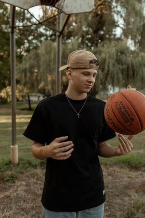 Person in black t-shirt poses with basketball outdoors in wooded setting showing different angles and stances.