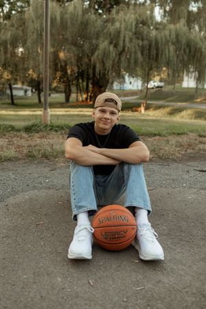 A person sits on a basketball court wearing jeans and a black shirt with a Spalding basketball beside them.