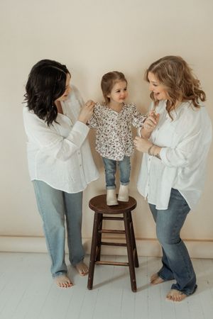 People in matching white shirts and jeans gather around a small child standing on a wooden stool against a light backdrop.