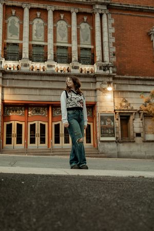 A person sits on a concrete ledge in front of a historic brick building with ornate architectural details at dusk.