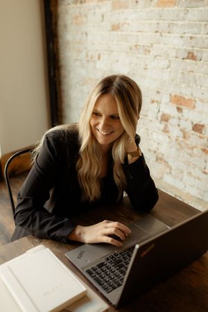 Professional working at wooden desk with laptop in modern industrial office with exposed brick wall.