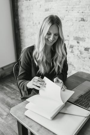 Black and white series of someone writing in notebook with laptop on wooden desk against brick wall background.