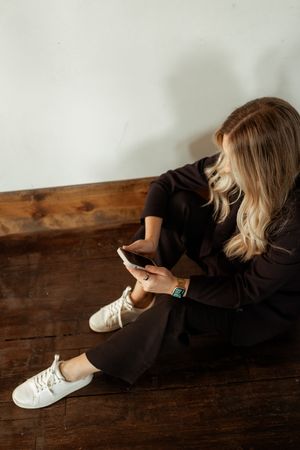 A casual business look featuring white sneakers and dark clothing while sitting on wooden flooring.