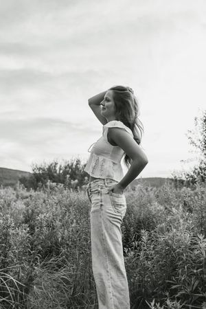 Black and white portrait of a woman in a tank top and jeans posing in a wildflower field at sunset.