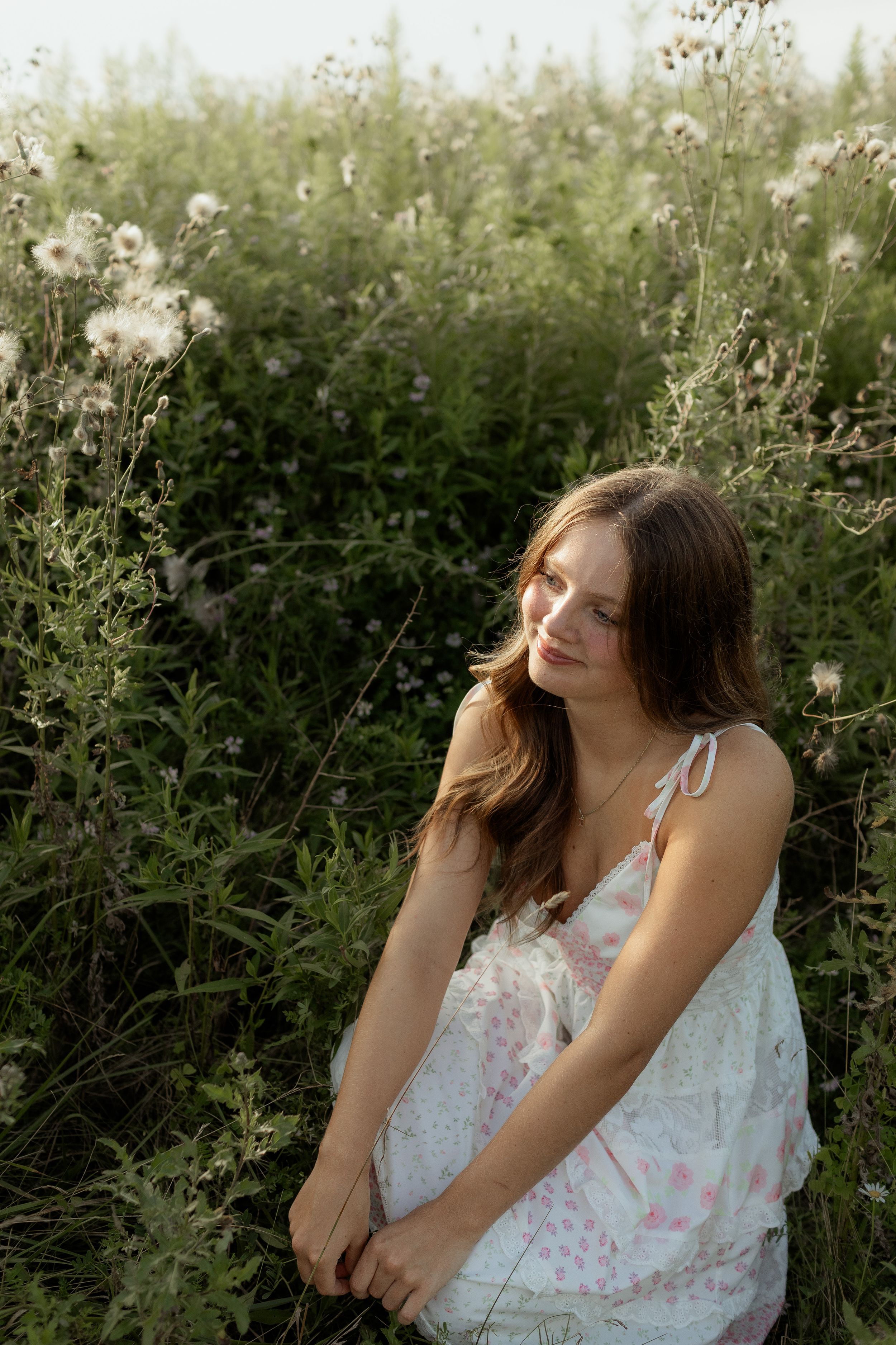 A dreamy outdoor portrait series in white floral dresses against lush green foliage creates an ethereal summer mood.
