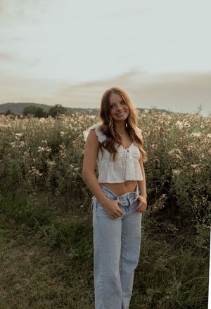 A person in light blue denim jeans poses in a wildflower field at sunset with a dreamy, ethereal atmosphere.