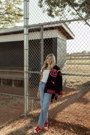 A person in jeans stands against a chain-link fence, showing off red and black sneakers in different poses.