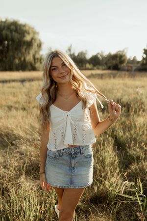 White crop top and denim mini skirt outfit photographed in golden hour sunlight in a grassy field.