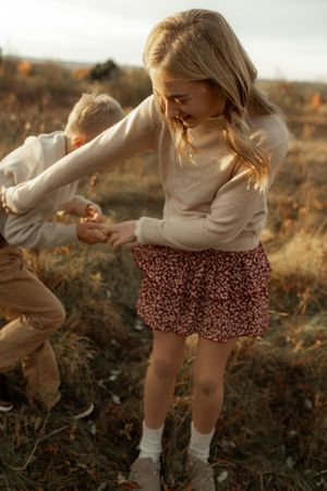 A series of photos showing a person in a cream sweater and floral shorts dancing playfully in a golden autumn field at sunset.