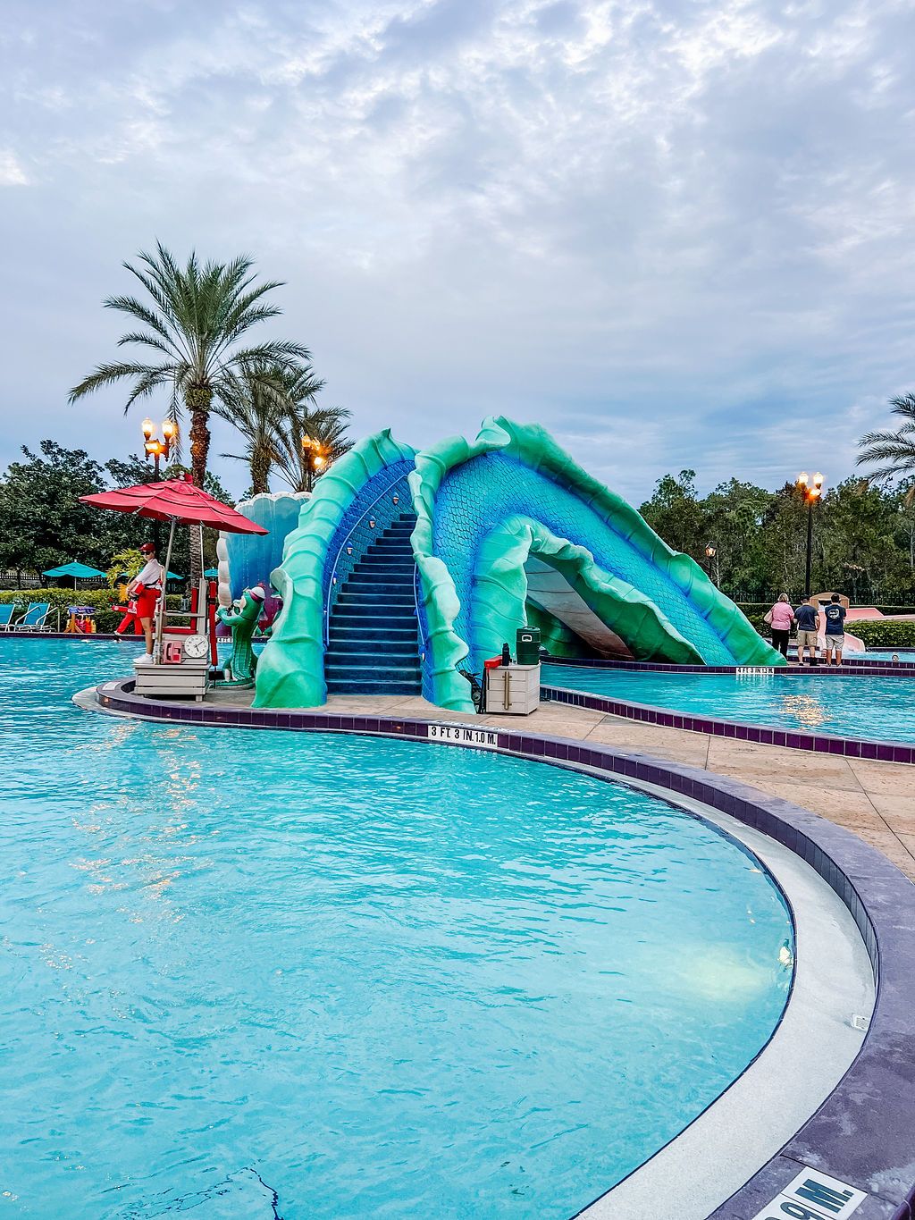 Large resort pool with turquoise water slides and palm trees.
