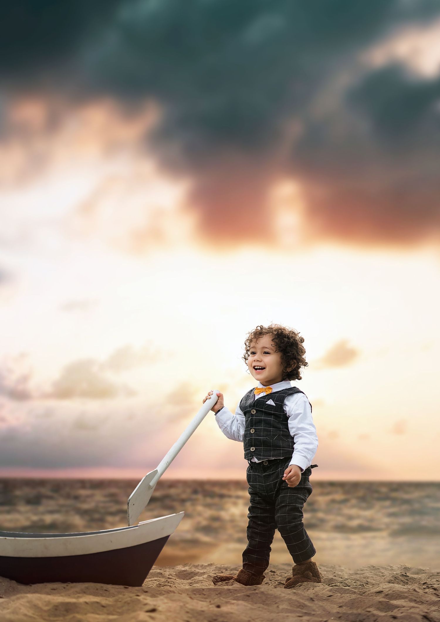 Toddler playing with toy boat on beach at sunset with dramatic sky.