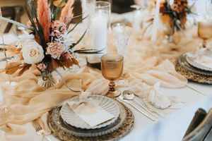 Elegant wedding table setting with peach-coloured tablecloth, woven chargers, and dried floral centrepiece at Nuddock Wood Lake