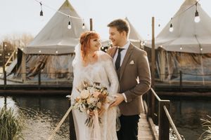 Elegant outdoor wedding celebration at Nuddock Wood Lake with teepee tents and romantic string lights along the water in the background.
