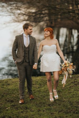 A couple in wedding attire walks hand in hand through a misty forest setting at Nuddock Wood Lake.