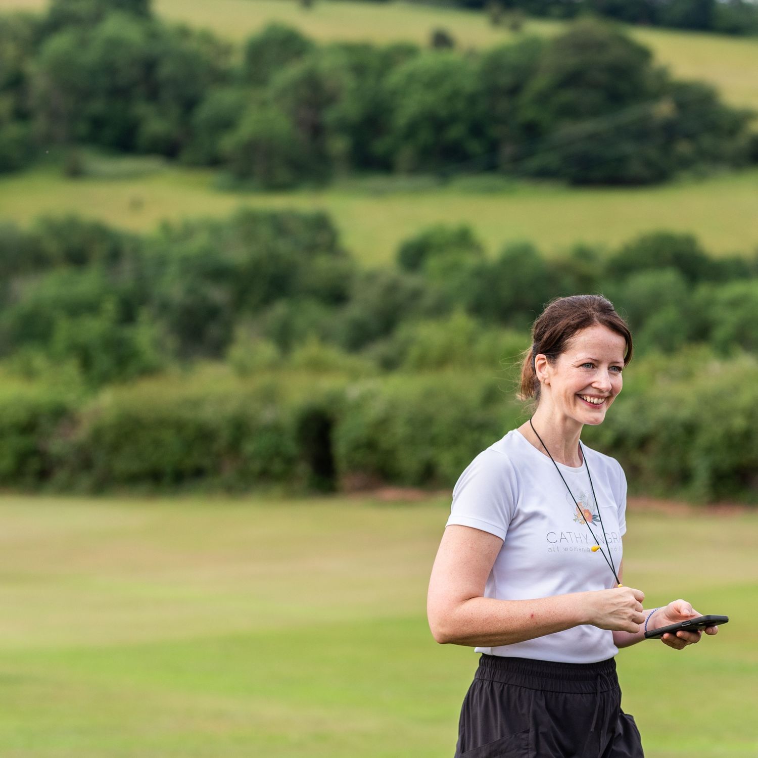 Person in white shirt outdoors against green rolling hills and trees.
