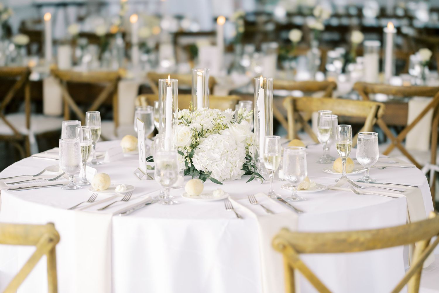 Elegant wedding reception tables decorated with white linens, floral centerpieces and vintage cross-back chairs.
