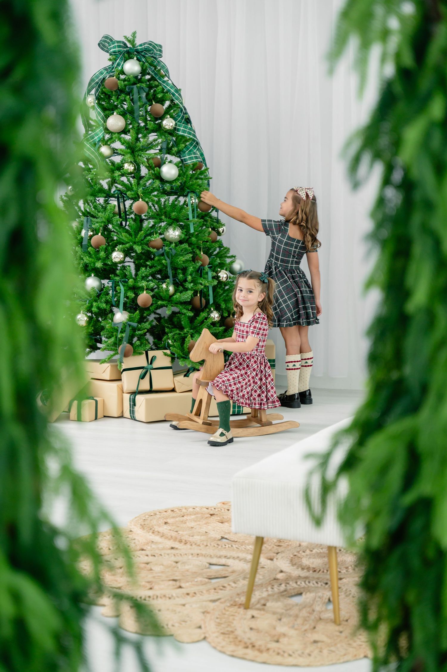 Three decorative trees next to each other with a white backdrop and children in plaid and polka dot dresses.