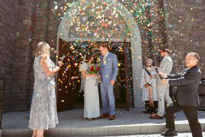 A couple celebrates under a stone archway while guests shower them with colorful confetti during a celebration.