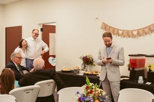 A reception event in a community room decorated with a banner and floral centerpieces on tables with white chairs.