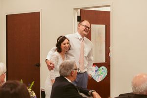 A couple laughs together while standing at a dinner reception in a room with brown walls.