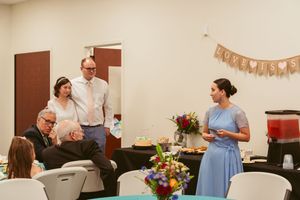 People gather in a wedding reception hall decorated with flowers and party decorations for a casual summer celebration.