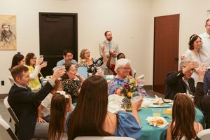 Wedding reception gathering in a church hall with guests seated at tables decorated with floral centerpieces.