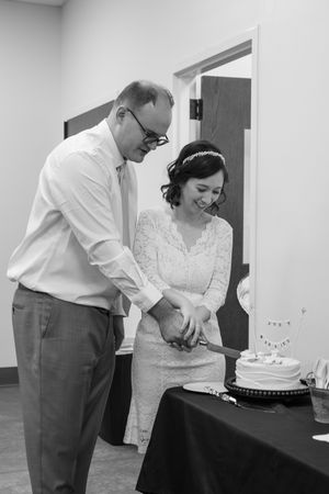 A couple cuts into their wedding cake together at an indoor reception venue.