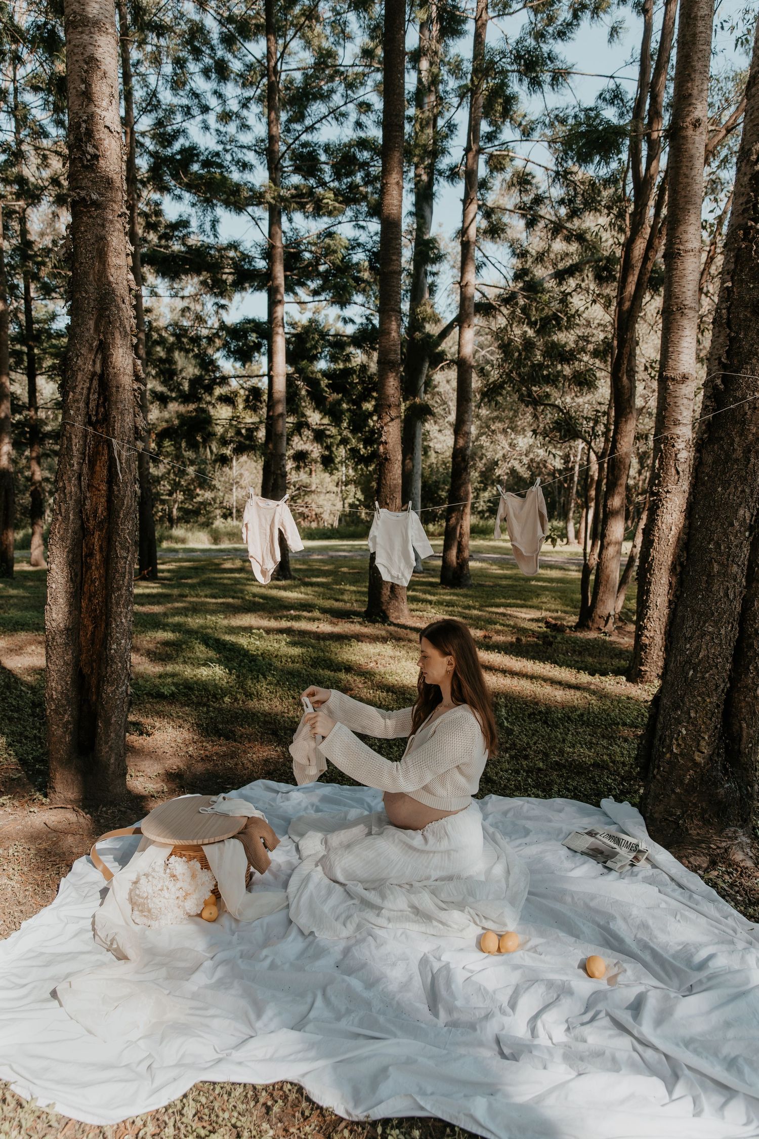 White flowing fabric spread across forest floor with pine trees in golden sunlight.