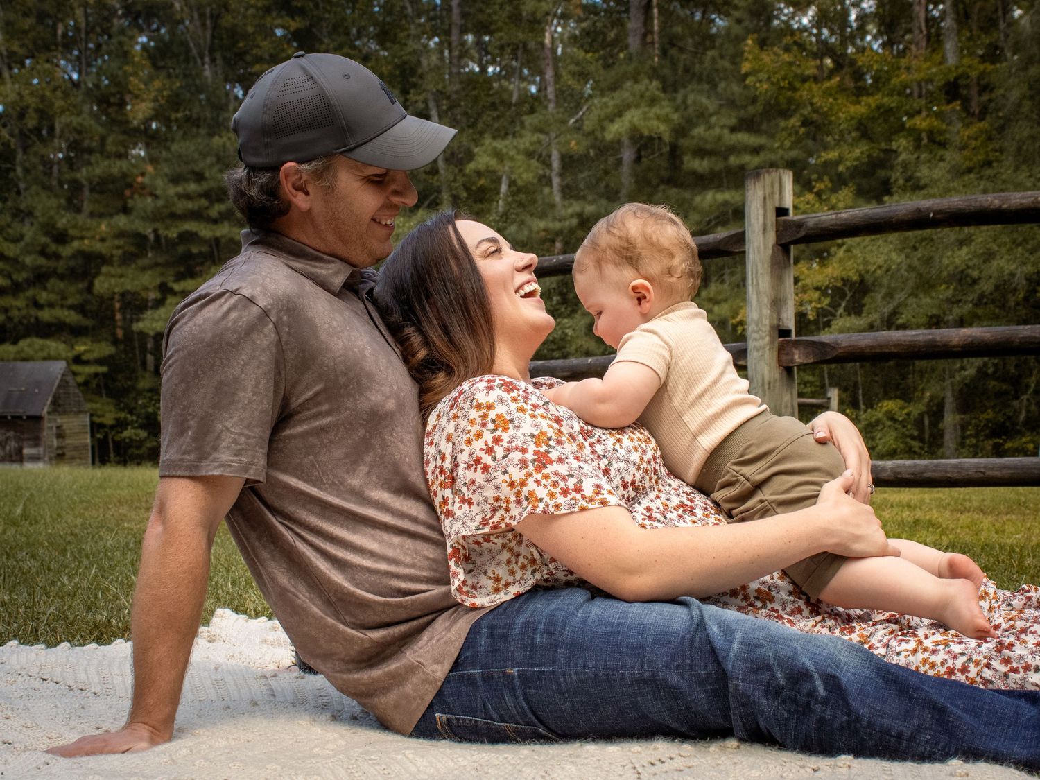 A touching outdoor photoshoot capturing tender moments between a couple in a lush meadow with wildflowers at sunset toddler embracing them.