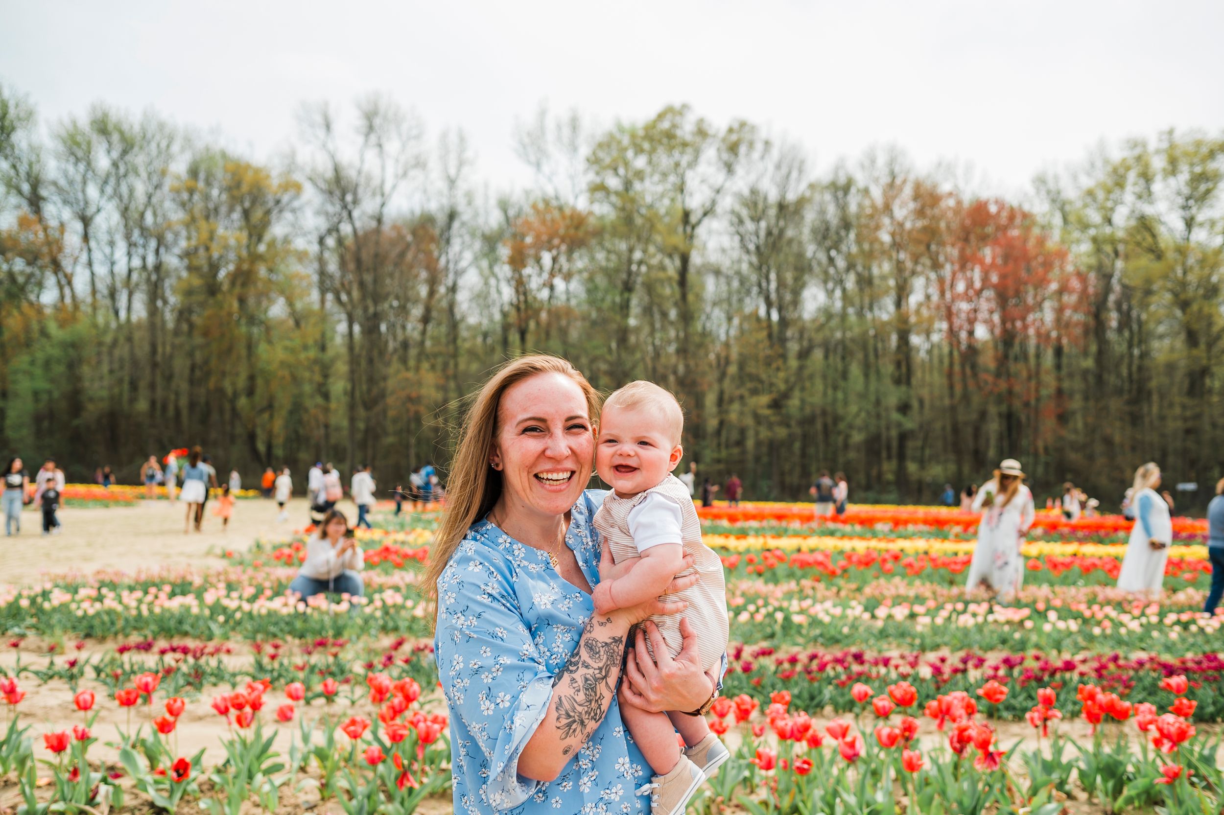 Mother and child walking through vibrant tulip fields in spring bloom with orange and pink flowers creating a scenic backdrop.