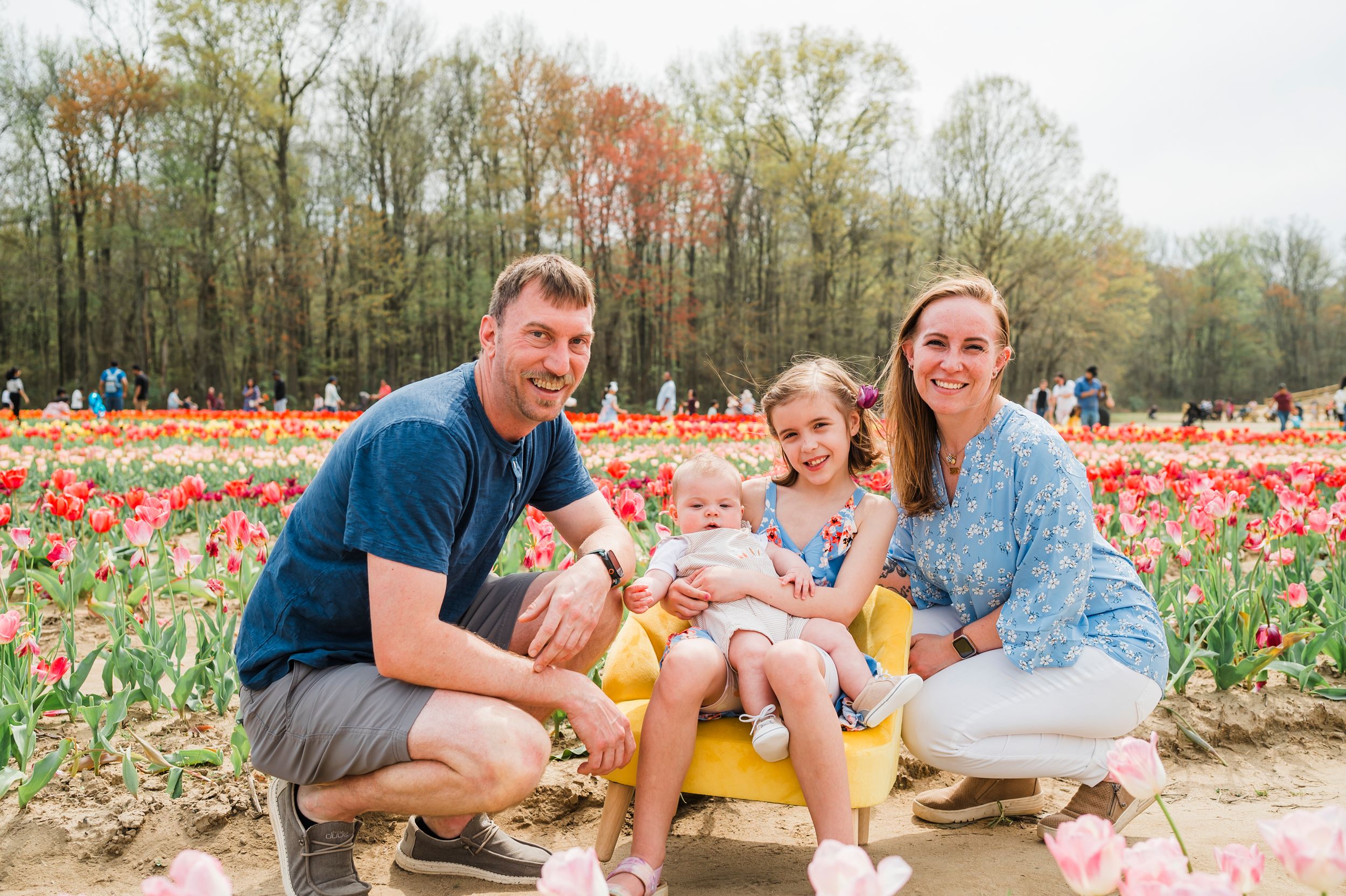 Three people sit together on a yellow bench at a colorful tulip field during springtime.
