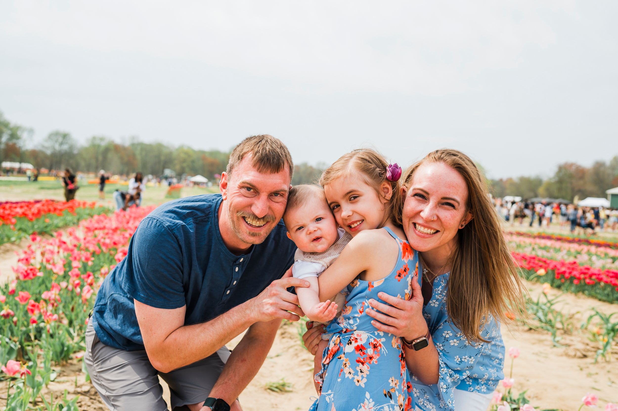A family poses together in a blooming tulip field on a sunny spring day.