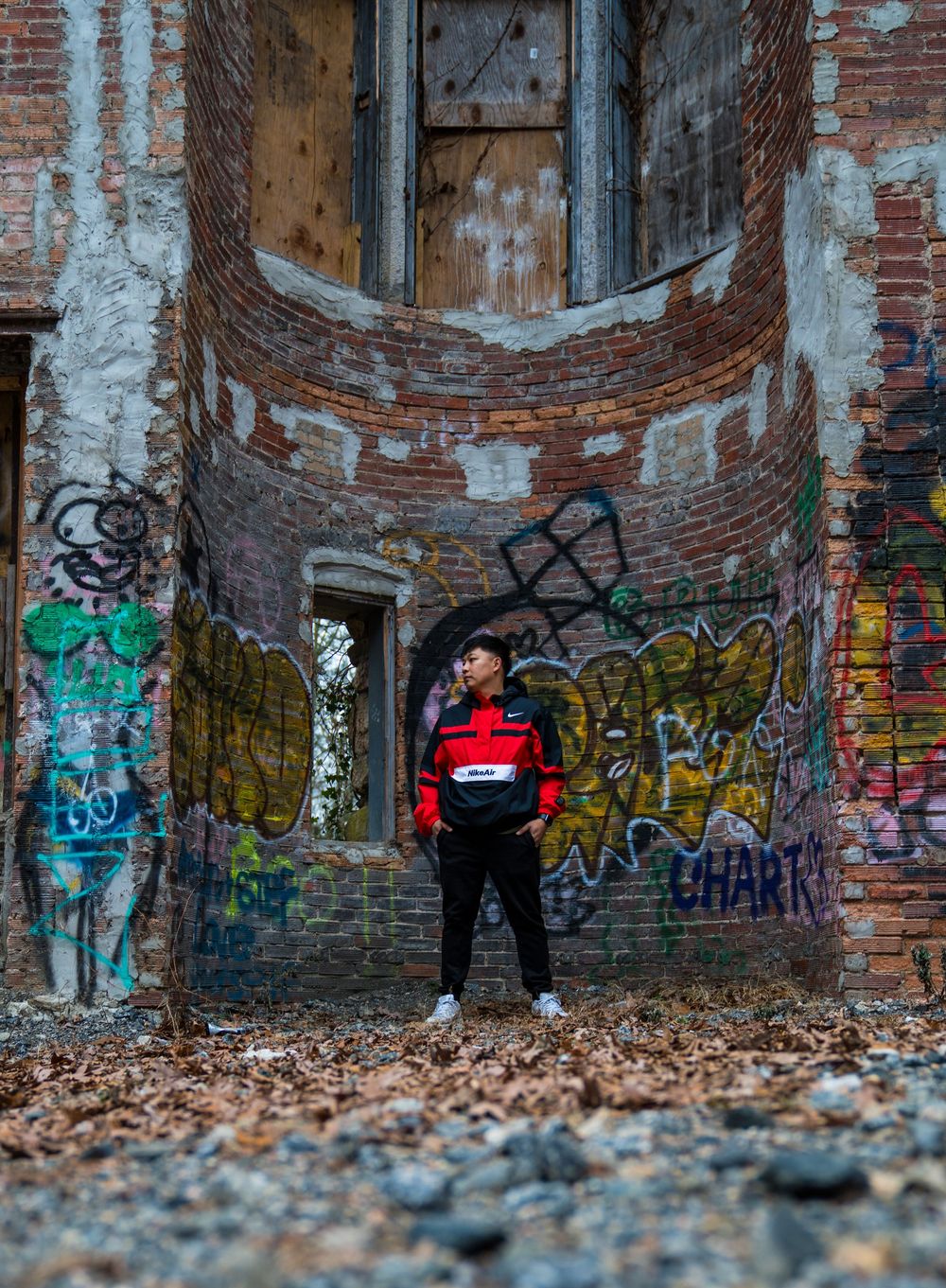 Atmospheric wide shot of urban decay with graffiti walls and figure in red jacket.