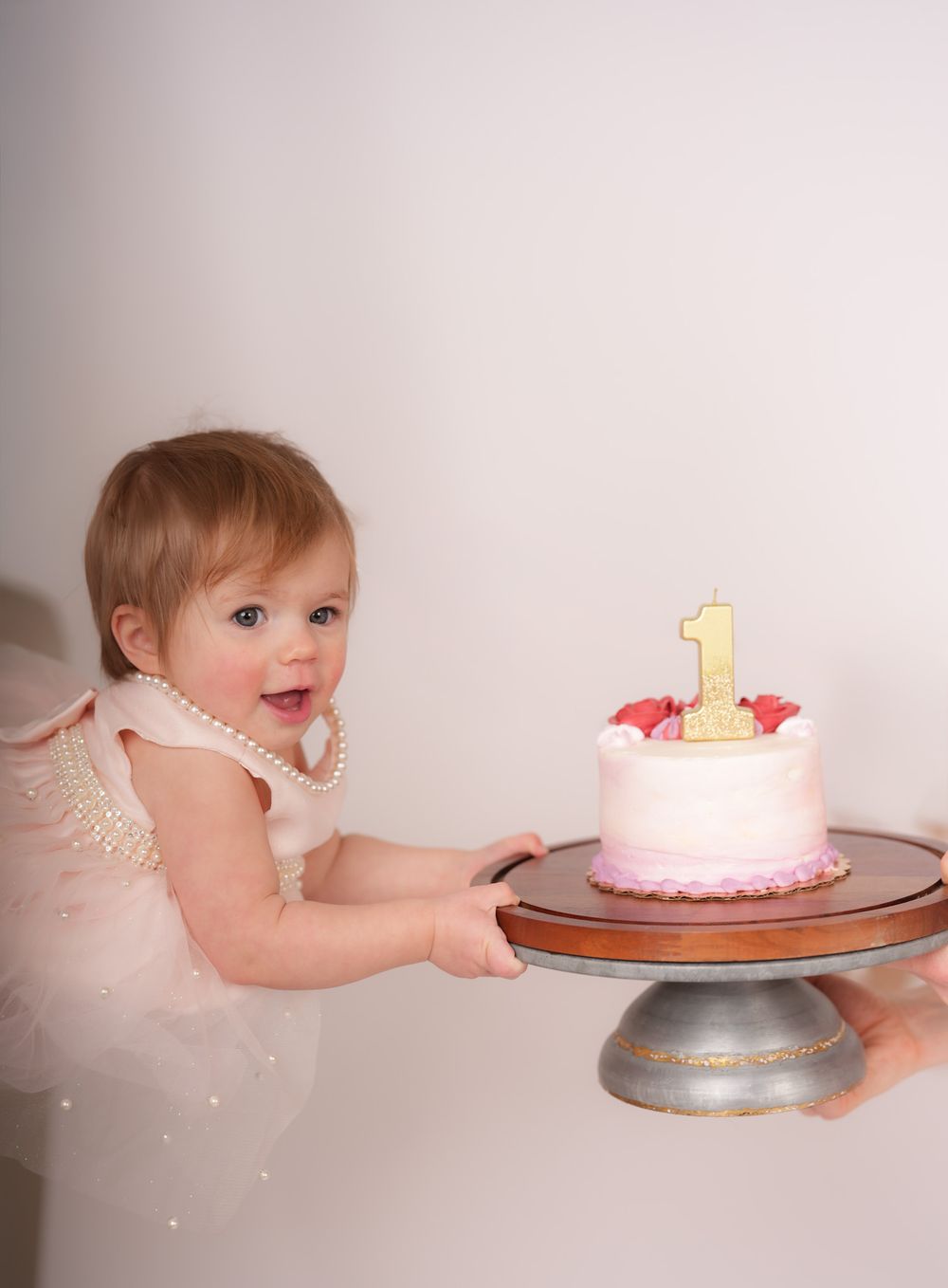 A series of photos showing a pink birthday cake with a gold number one candle being smashed and eaten.