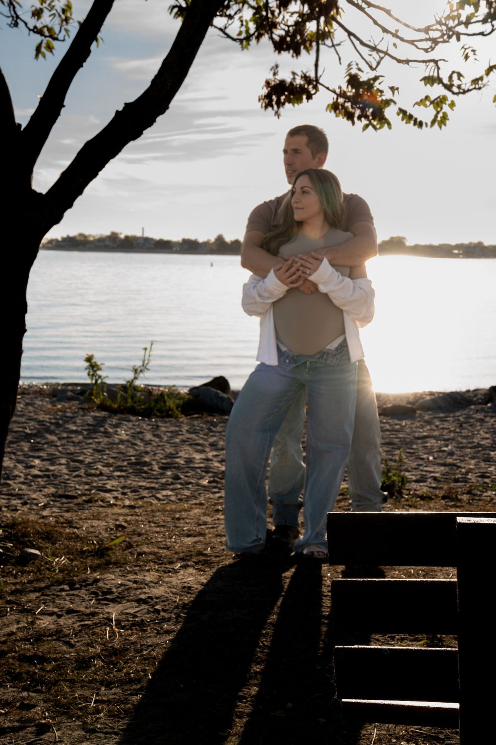 Couple sitting together on a rocky beach at sunset with water in the background.