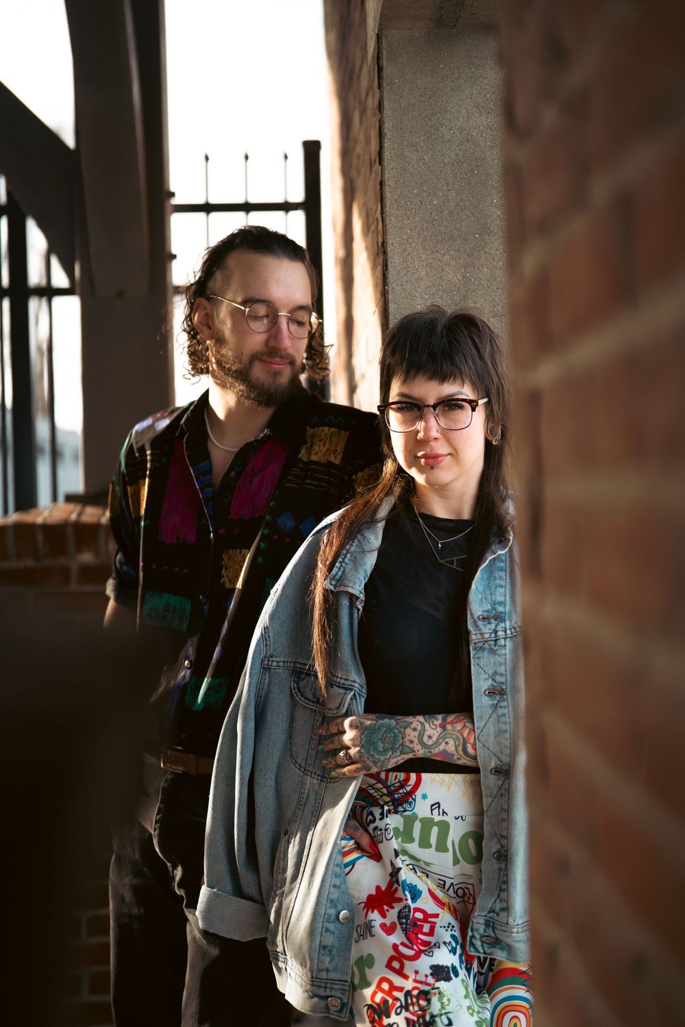 A couple in casual attire poses together in an industrial space with brick walls and natural lighting. Engagement photo shoot