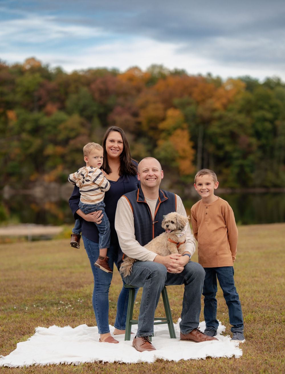 Family group sits together on white blanket outdoors with their small dog during fall season. Family Photoshoot. Family Photographer